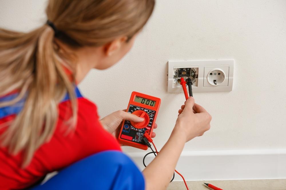 Young,Female,Electrician,Measuring,Voltage,Of,Socket,At,Home