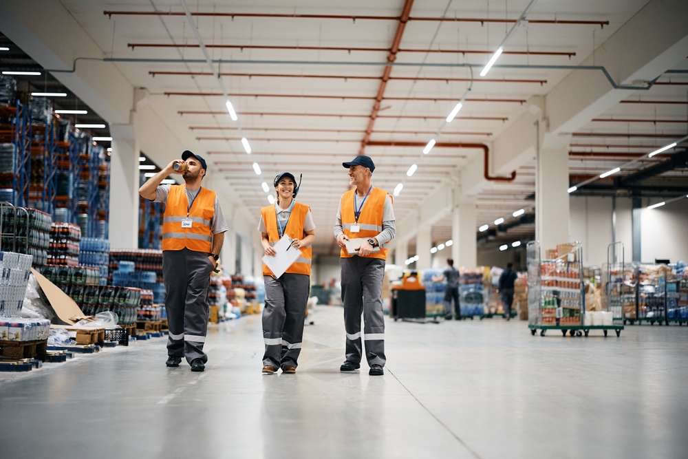 Happy,Warehouse,Worker,And,Her,Male,Coworkers,Walking,Through,Distribution